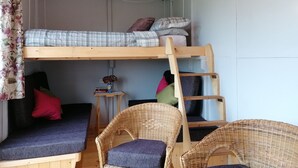 En våningssäng med en stege, ett litet bord med en vas och flätade stolar.