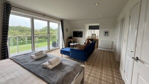 A hotel room with a bed, a sofa, a TV, and a balcony with a view.