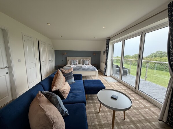 A spacious room with a large bed, a blue sofa, a small table, and a balcony with a view.