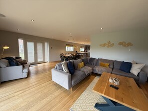 Uma sala de estar moderna com um sofá cinzento, uma mesa de centro de madeira e uma área de jantar ao fundo.