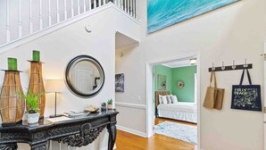 A staircase with a white railing, a console table with decorative items, a mirror, and a wall with a painting and a coat rack. - Folly Beach Gem: Walk to Beach, Restaurants & Nightlife - Happy Ours (Folly Beach)
