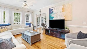 A spacious living room with a large flat-screen TV, a wooden coffee table, and a comfortable seating area with sofas. - Folly Beach Gem: Walk to Beach, Restaurants & Nightlife - Happy Ours (Folly Beach)