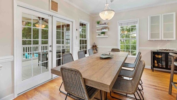 A dining room with a large wooden table, wicker chairs, and a chandelier. There are glass doors leading to an outdoor area with a pool. - Folly Beach Gem: Walk to Beach, Restaurants & Nightlife - Happy Ours (Folly Beach)