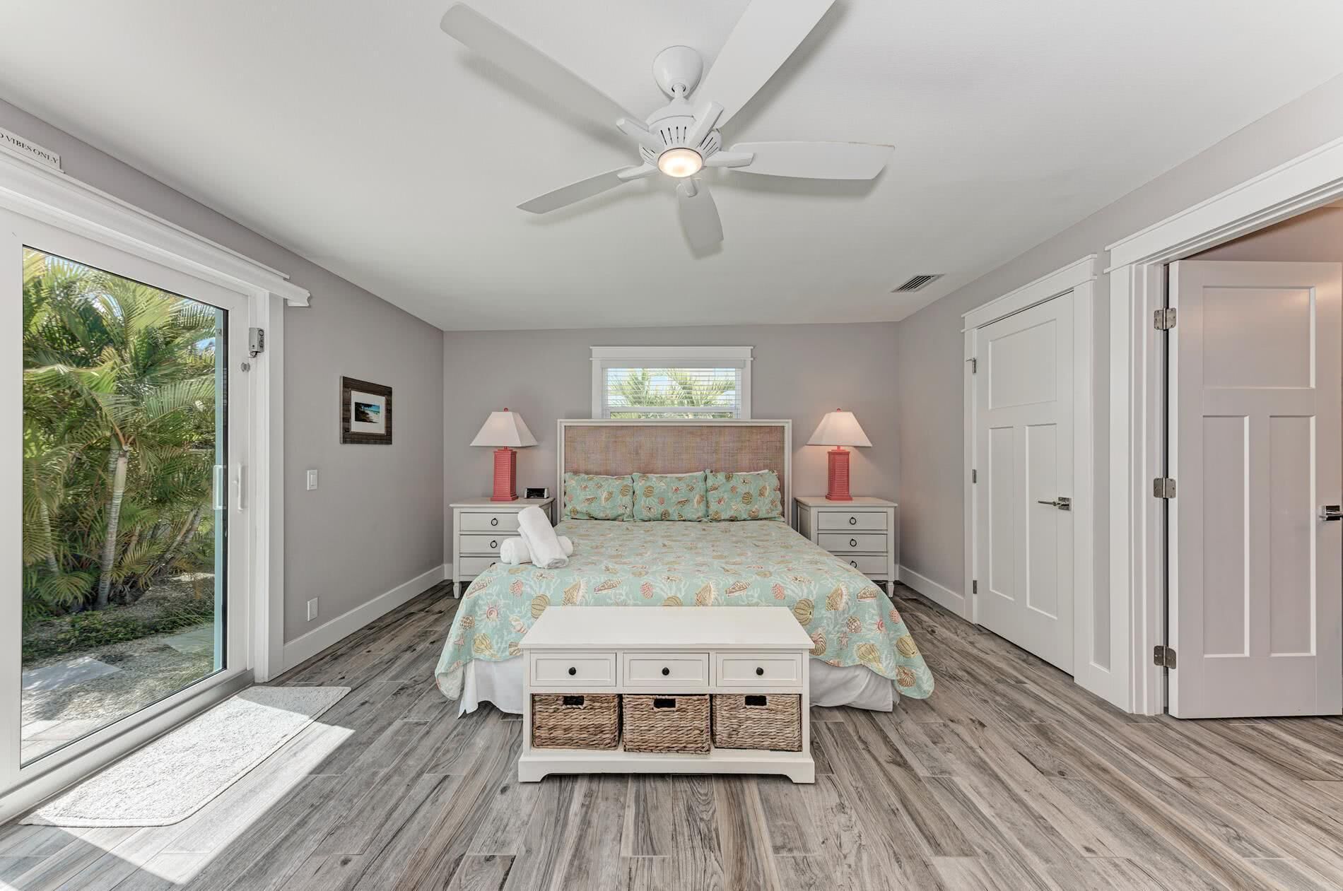 A bedroom with a bed, two bedside tables, a ceiling fan, a window, and a door.