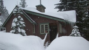 Una cabaña de troncos con techo y ventanas cubiertas de nieve, rodeada de árboles nevados.
