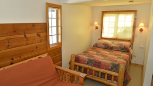 Un dormitorio con cabecera de madera, una cama individual con colcha, dos lámparas fijadas a la pared y una ventana con persianas.
