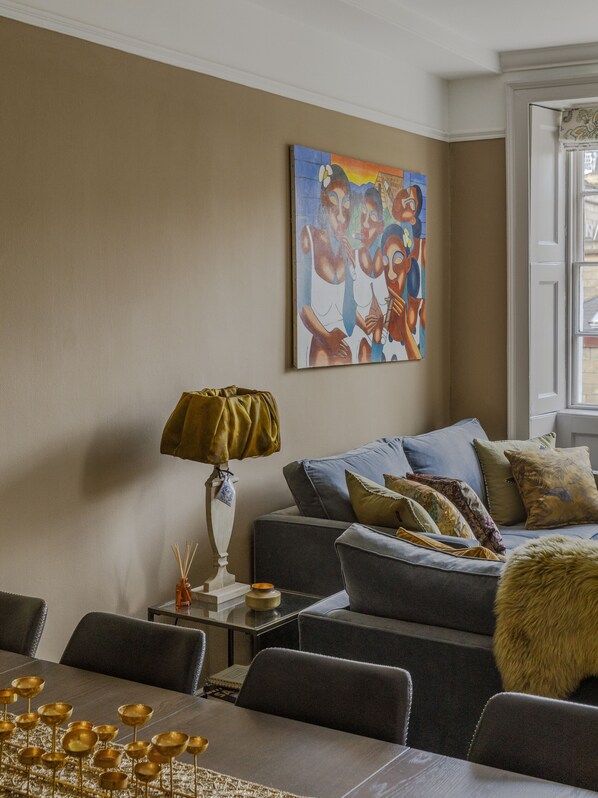 Un salon avec un canapé, une table sur laquelle sont posés des bols dorés, une lampe et un tableau accroché au mur.