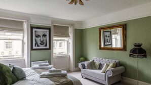 A bedroom with a bed, a grey sofa, a floor lamp, and artwork on the walls. - Impeccable 4-bed Apartment in Bath (Bath)