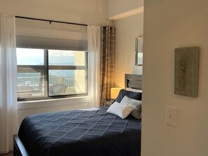 Ein Schlafzimmer mit großem Fenster, einem Bett, einem Nachttisch und einem Gemälde an der Wand.