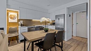 Une cuisine moderne avec des meubles blancs, un réfrigérateur en acier inoxydable et un coin repas comprenant une table et des chaises en bois.