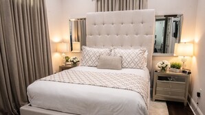 A large bed with a tufted headboard, two bedside tables with lamps, and a mirror above the bed. - Mid City Gorgeous Custom 4/3 one block from Street Car (New Orleans)