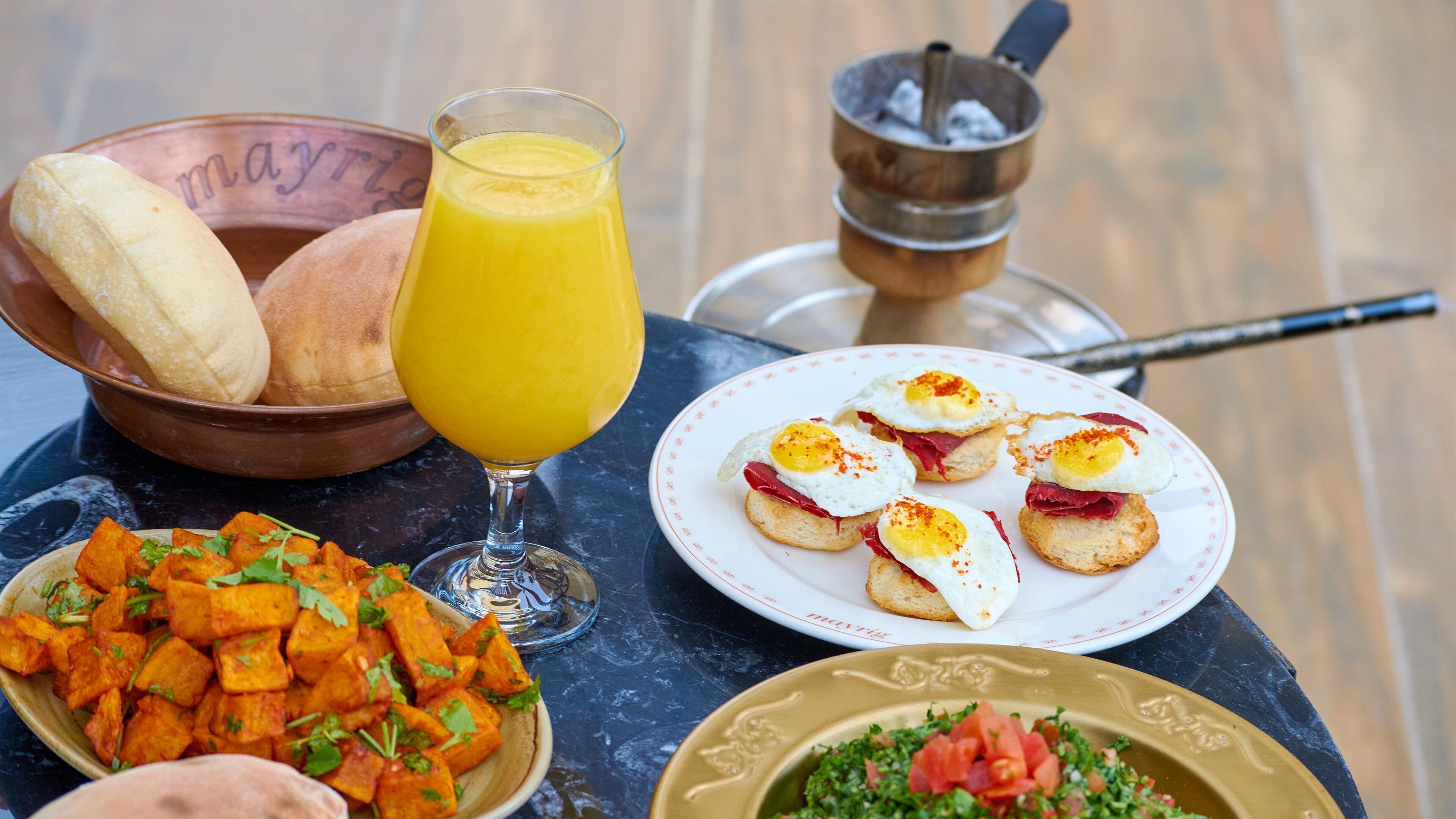 Ein Esstisch mit Brot, Orangensaft, einer Eierschale und einer Schüssel geröstetem Gemüse.