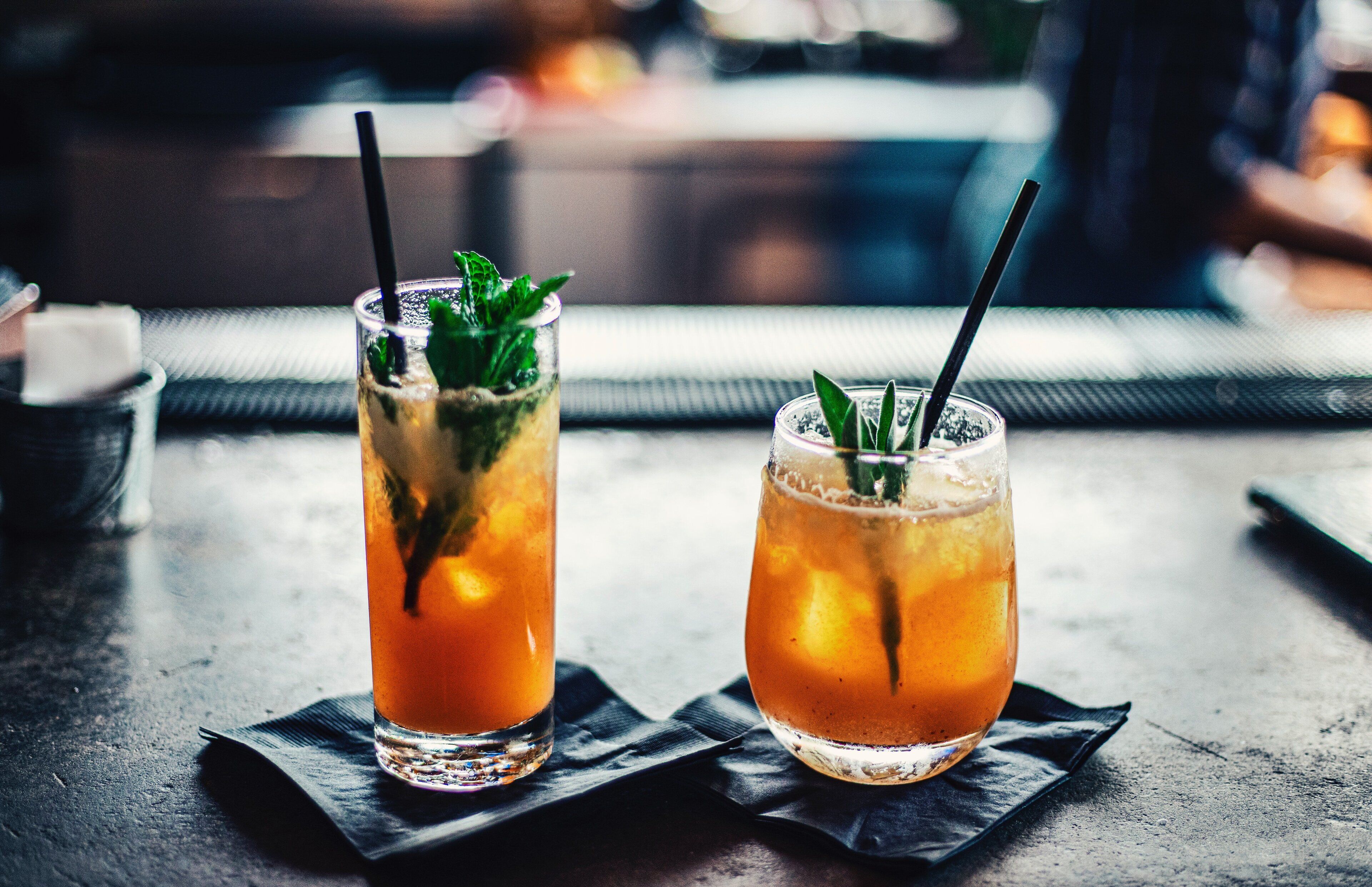 Two glasses of iced tea with straws and mint leaves on a table.