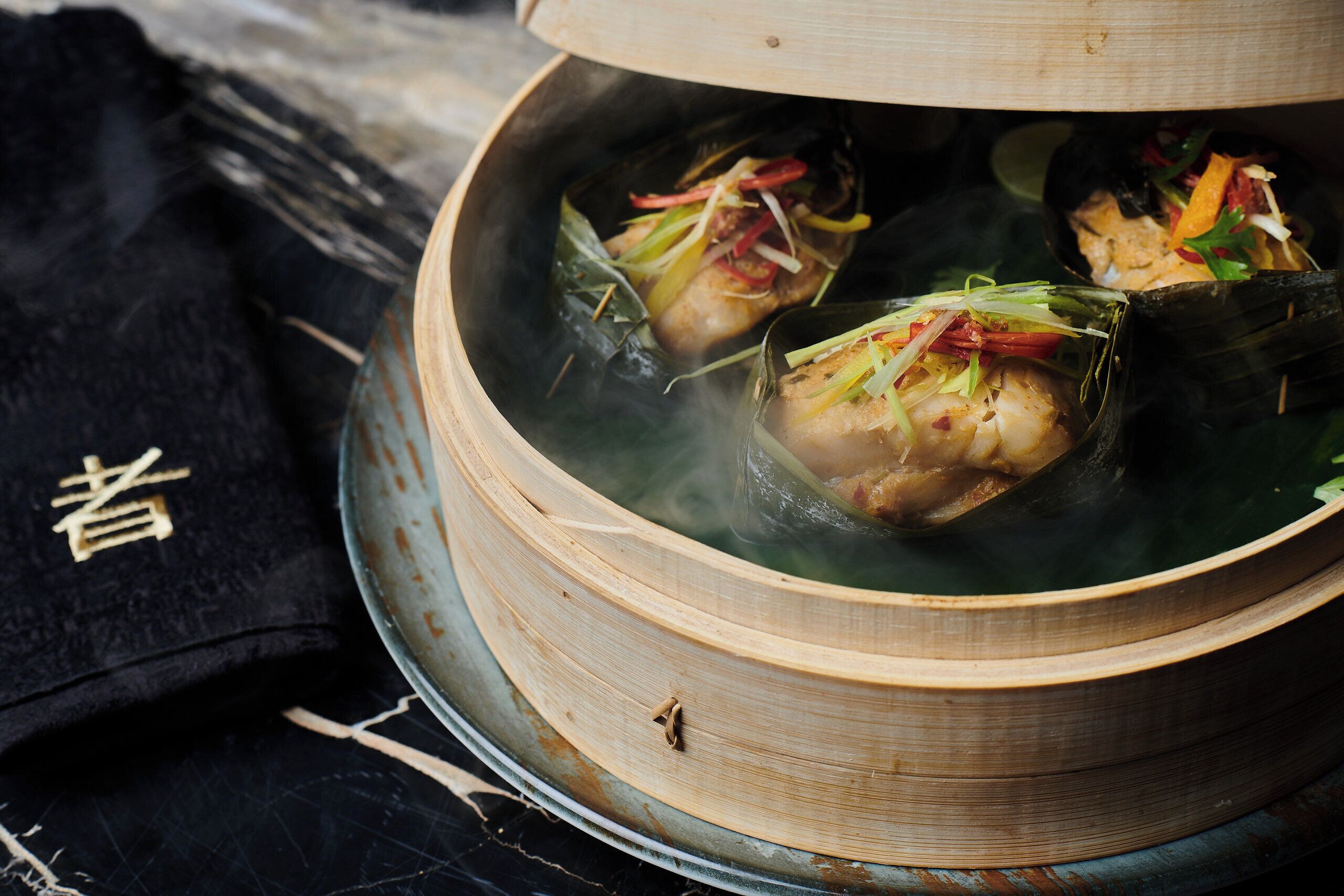 A traditional cooking pot with a lid, containing food wrapped in leaves, placed on a surface with a black cloth and a wooden object with Chinese characters.