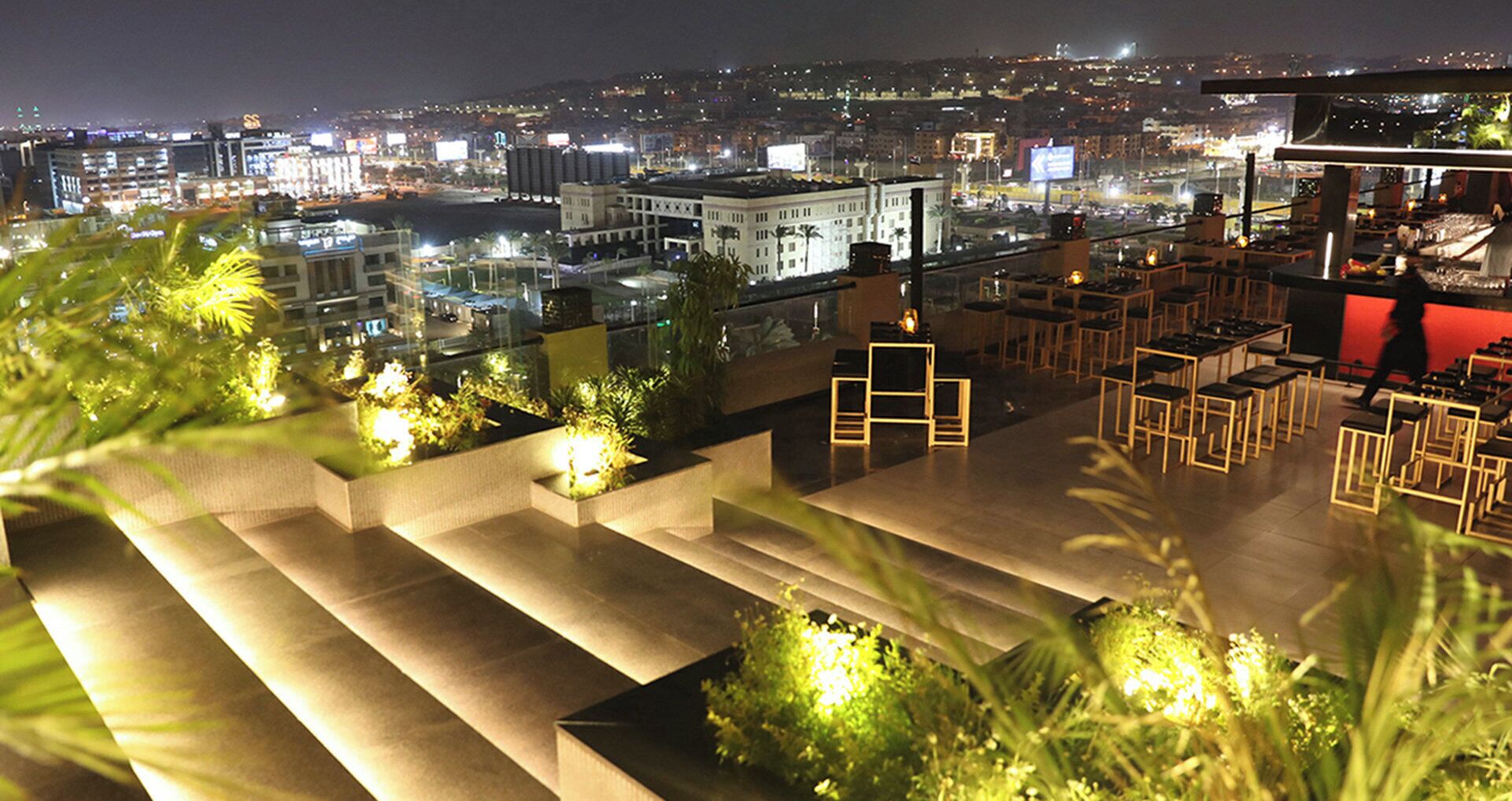 Terraço no telhado com mobiliário externo e vista para a cidade à noite.