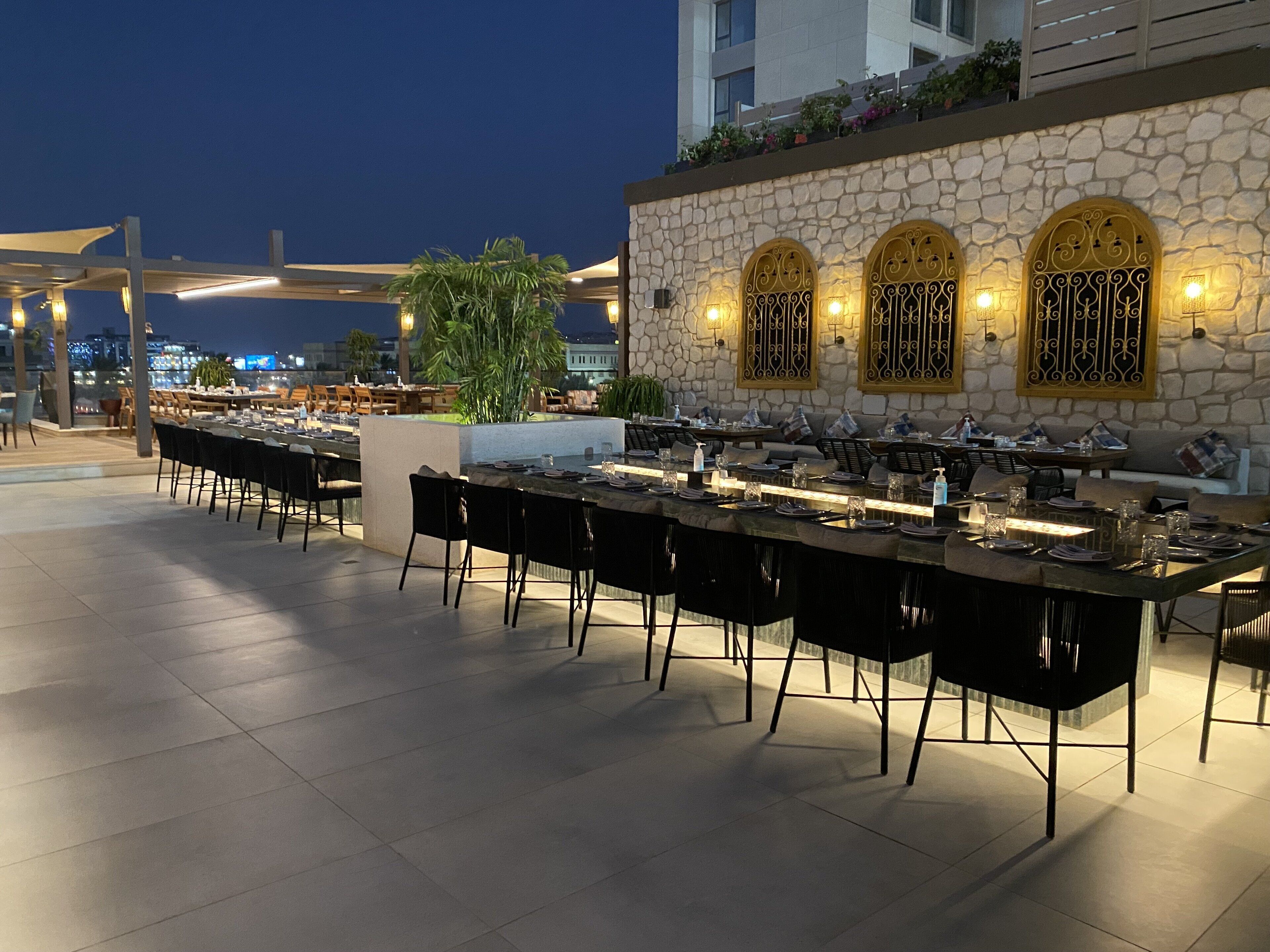 An outdoor dining area with stone walls and arched windows, equipped with tables and chairs.