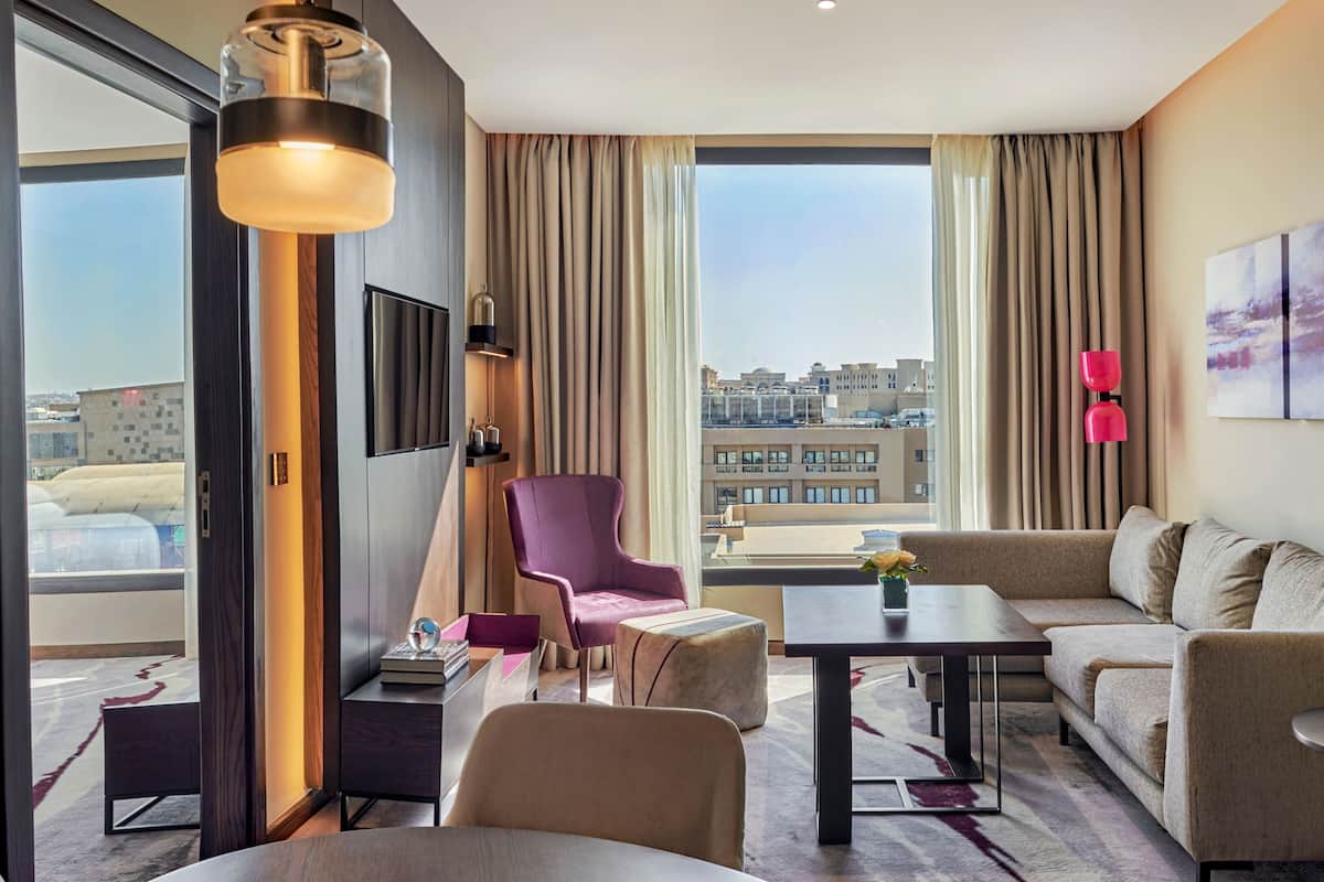 Une chambre d’hôtel moderne avec une grande fenêtre, un canapé, un fauteuil, une table et une lampe.