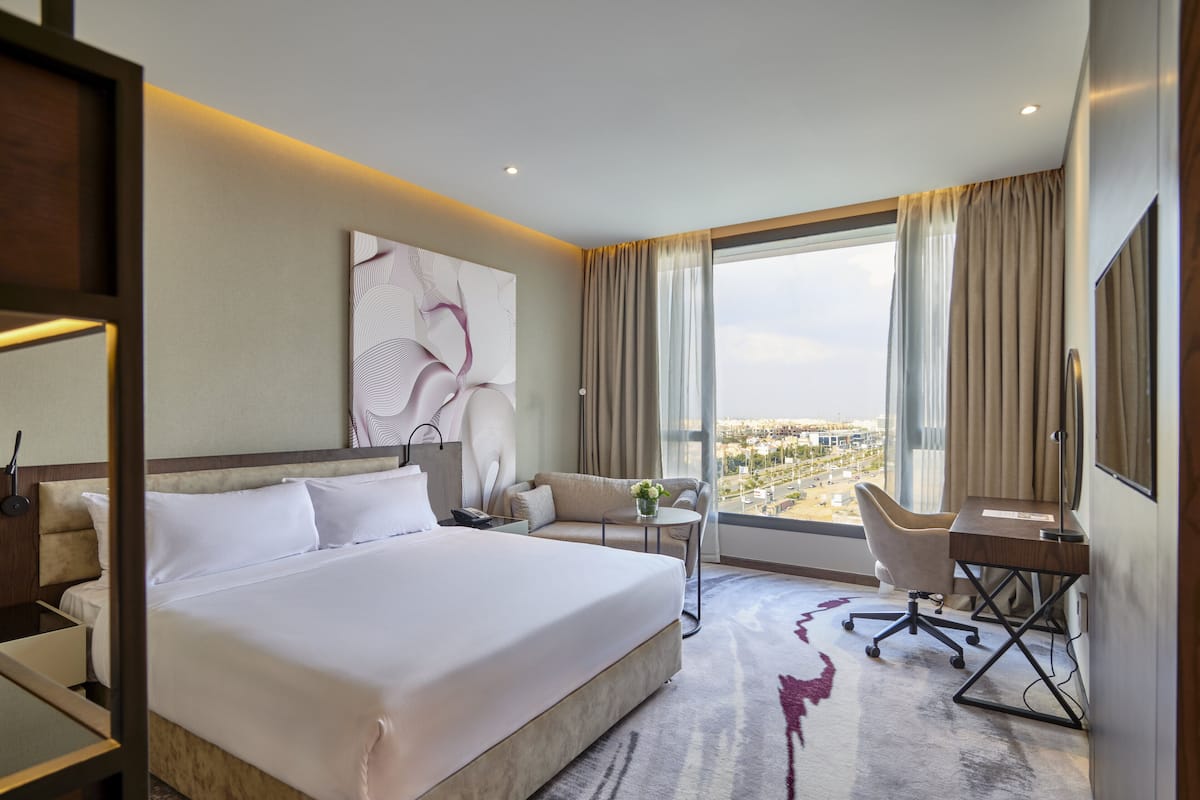 Une chambre d’hôtel avec un grand lit, un bureau, une chaise, un canapé et une vue sur la ville.