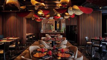 Interior de restaurante con mesas redondas, sillas y lámparas colgantes.