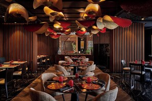 Een restaurantinterieur met ronde tafels, stoelen en hangende lampen.