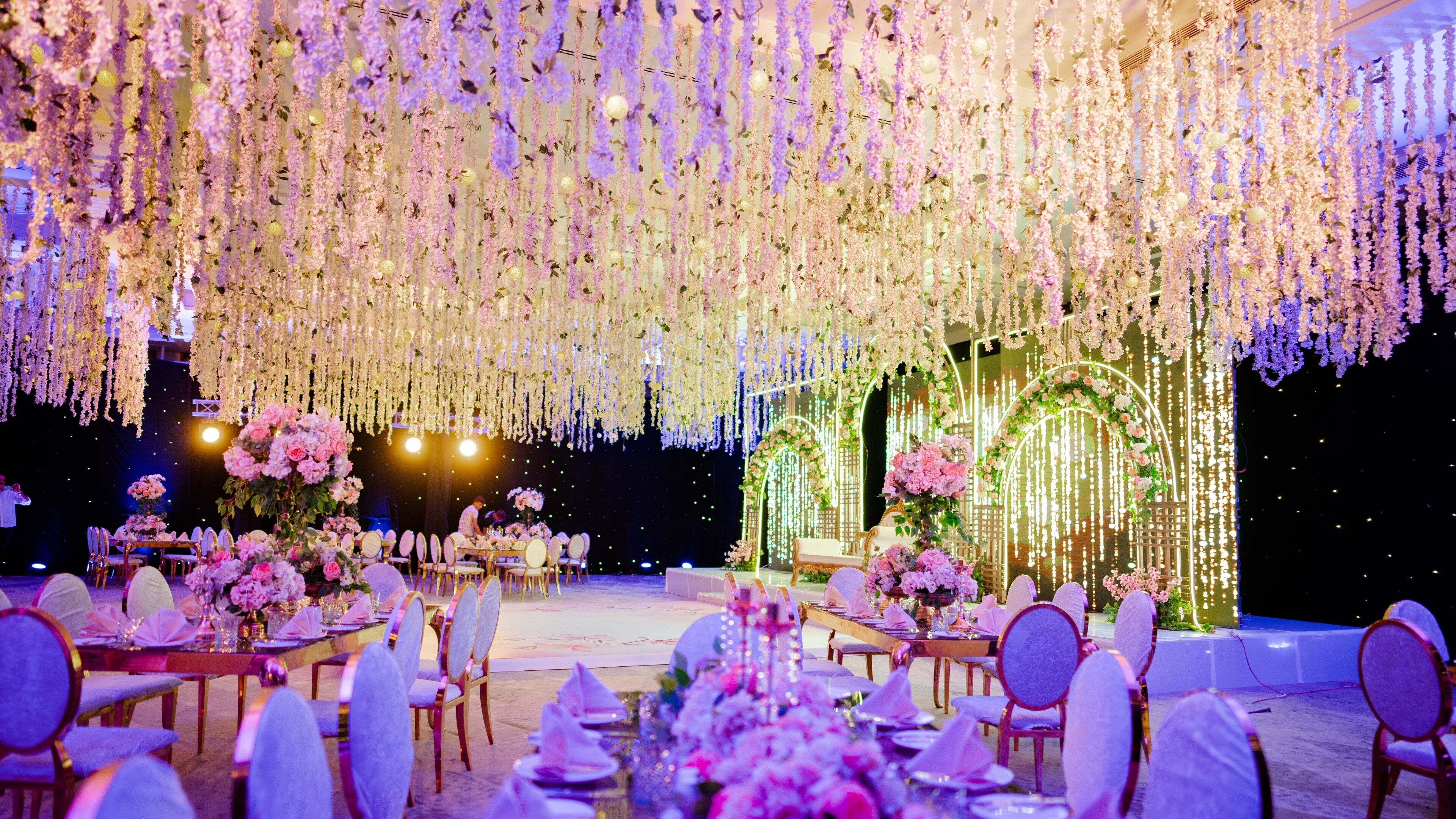 A banquet hall with round tables, chairs, and a stage with floral decorations.