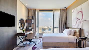 A hotel room with a bed, a desk, a chair, a TV, and a large window with a city view.