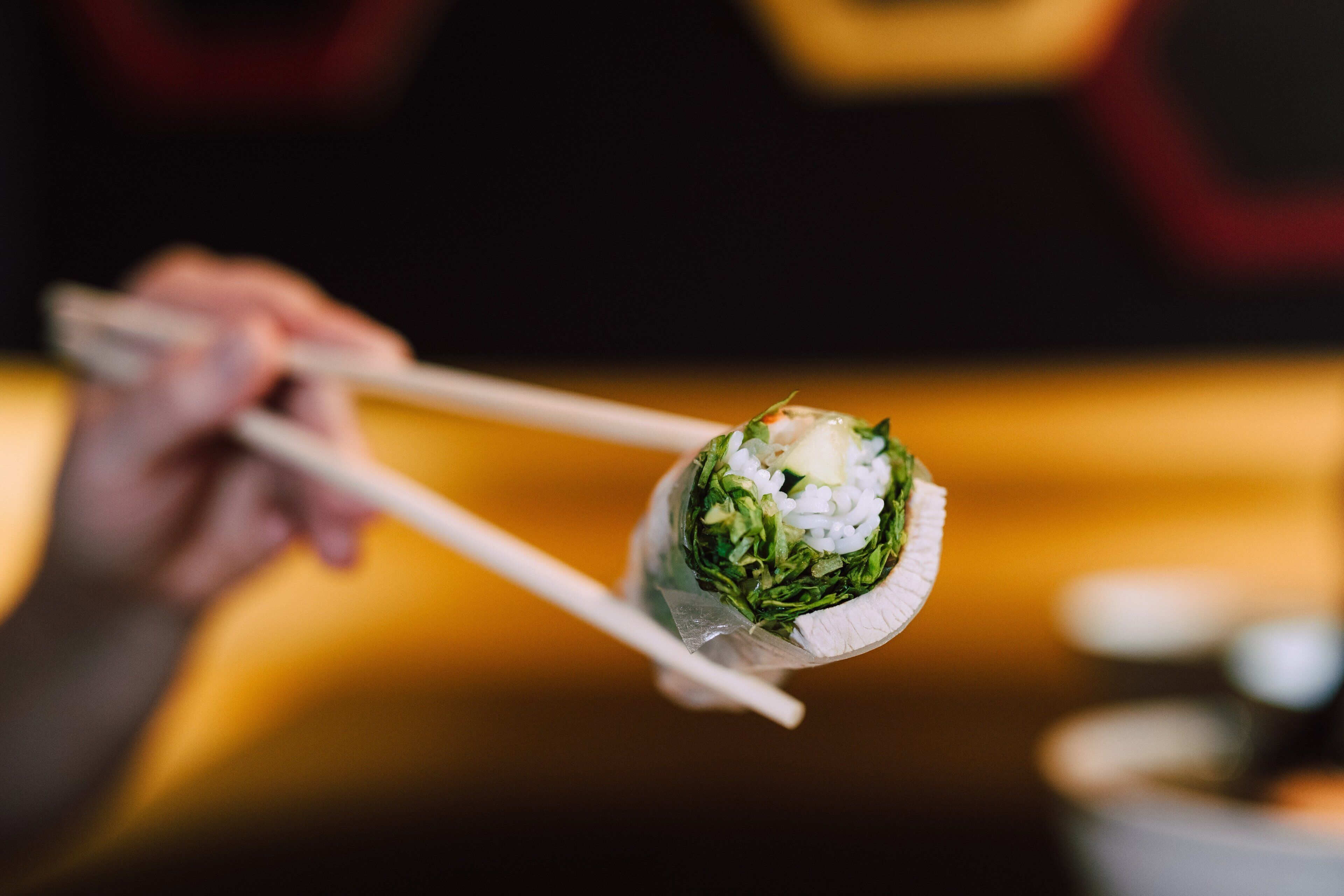 A person holding a sushi roll with chopsticks.