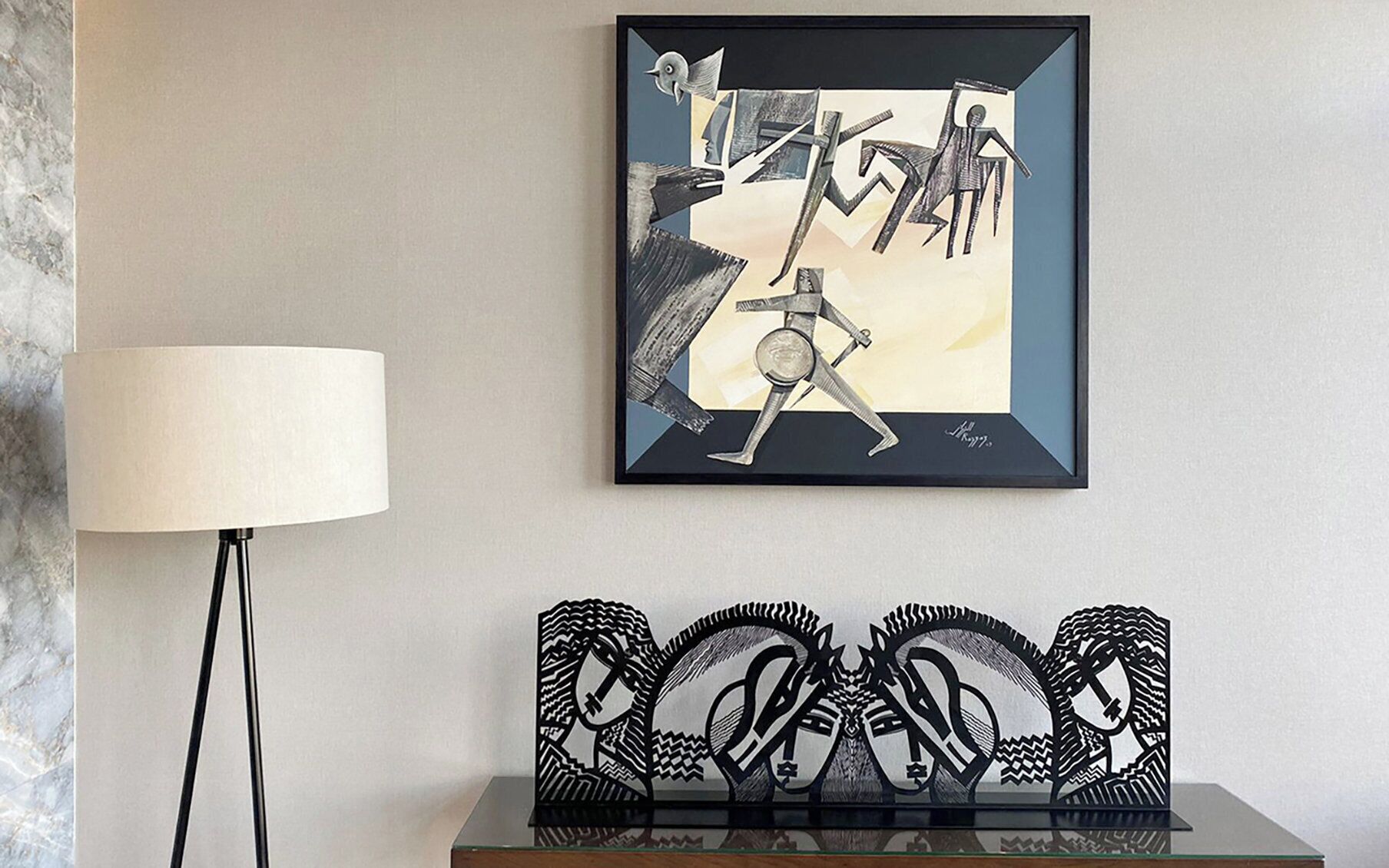 A framed abstract artwork on a wall, a floor lamp, and a decorative black metal piece with geometric shapes.