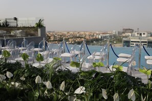 Un espace piscine aménagé sur le toit, avec des chaises transparentes et une vue sur le paysage urbain.