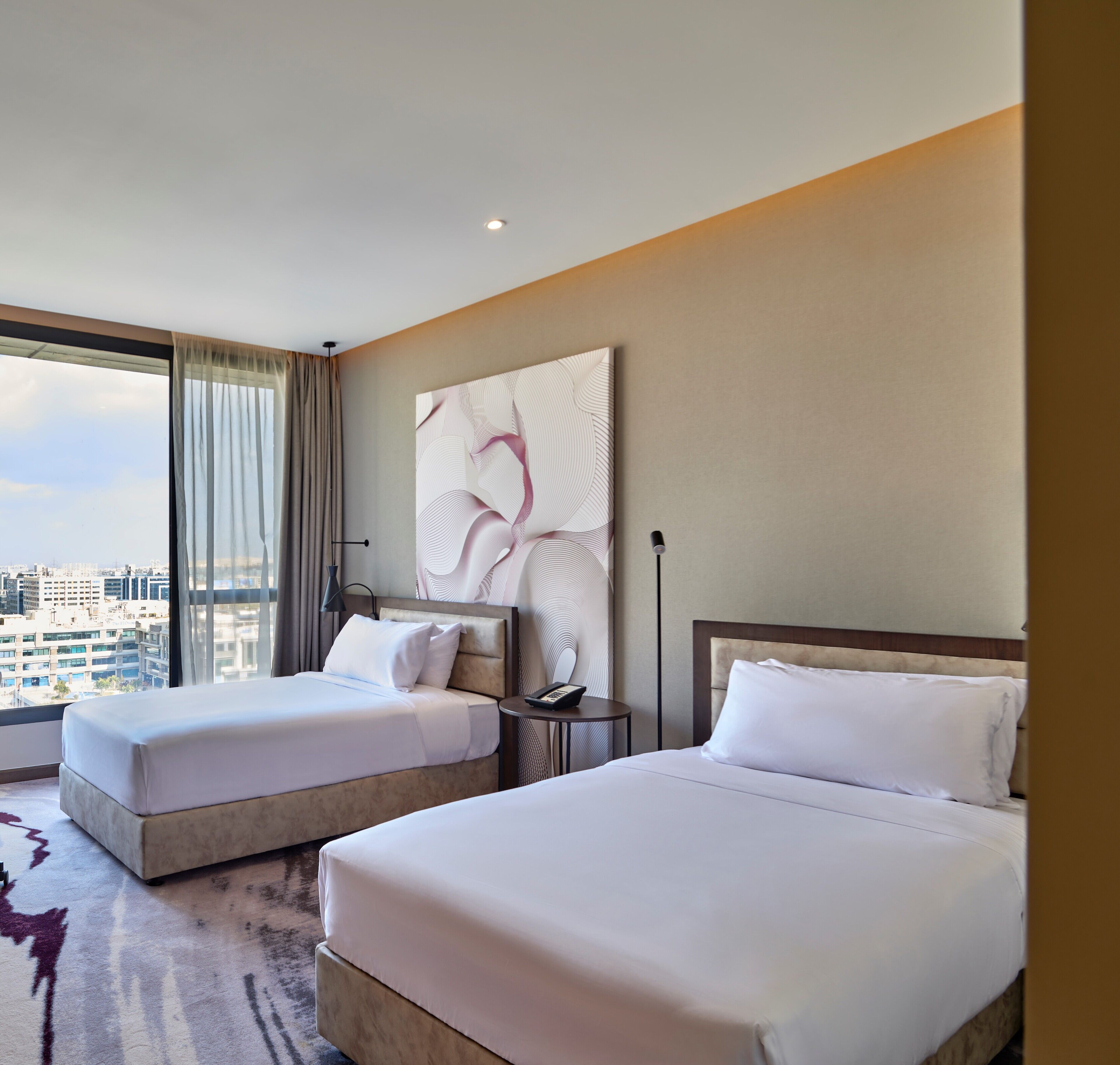 A hotel room with two beds, a city view, a large abstract painting, and a modern design.