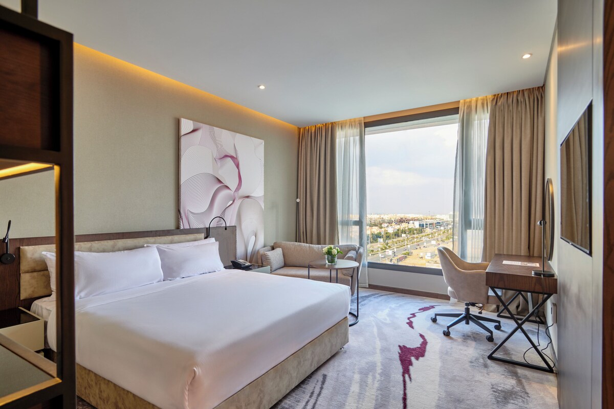 Une chambre d’hôtel avec un grand lit, un bureau, une chaise, un canapé et une vue sur la ville.