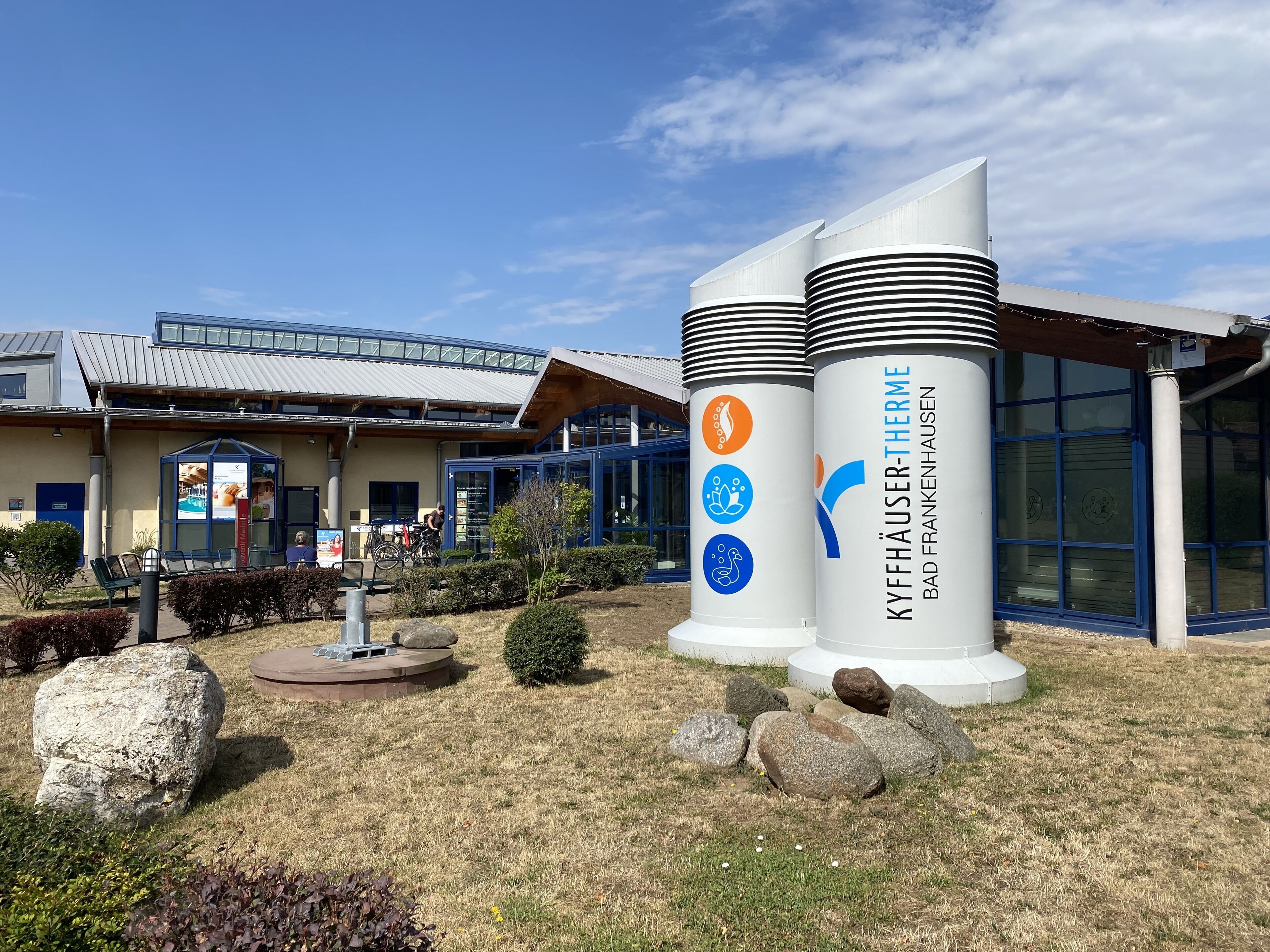 Een gebouw met een modern architectonisch ontwerp, met een glazen gevel en een opvallende cilindervormige structuur met signage.