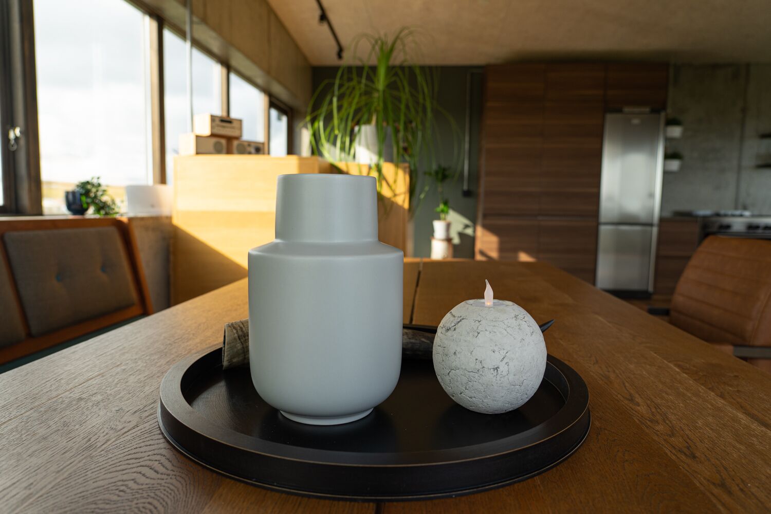 A modern kitchen with a wooden table, a white vase, and a spherical candle on a black tray.