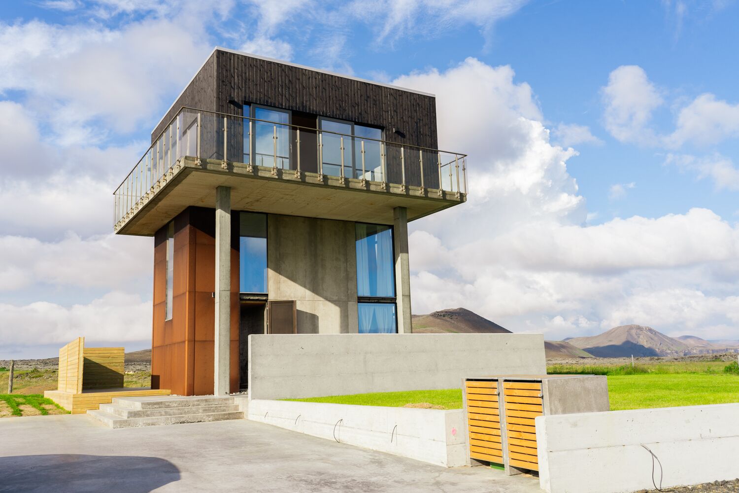 A modern two-story building with a balcony, large windows, and a concrete base.