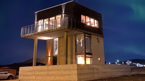Un bâtiment à deux étages doté d’un balcon, sous un ciel nocturne où l’on peut voir des étoiles et des aurores boréales.