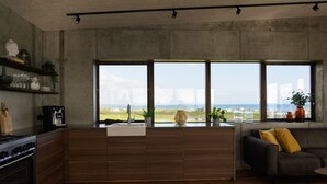 Une cuisine moderne dotée d’un grand îlot central, de meubles en bois et offrant une vue sur la mer grâce à de grandes fenêtres.