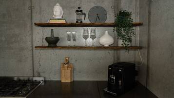 Une cuisine équipée d’une cuisinière à gaz, d’une machine à café, d’une horloge et de divers ustensiles de cuisine rangés sur des étagères.