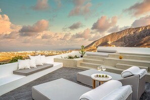 Una terrazza panoramica sul tetto con un'area salotto, un tavolo con bicchieri e frutta, e vista sulla città e sulle montagne.