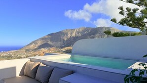 A rooftop terrace with a pool, seating area, and a view of a mountainous landscape.