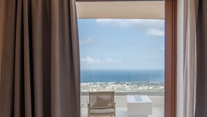 A hotel room with a bed, a view of the sea, and a balcony with a chair and table.