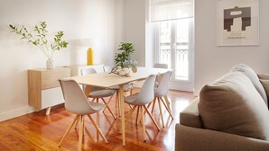 Ein modernes Wohnzimmer mit Holzboden, einem Esstisch mit Stühlen, einer Couch und einem großen Fenster mit Balkon.
