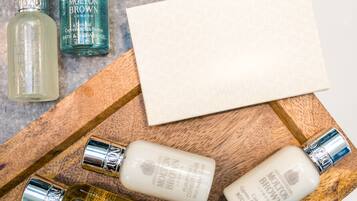 A wooden tray with various bottles of Molton Brown personal care products, including a bath and shower gel, a body lotion, and a shampoo.