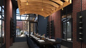 A modern dining area with a long table set for a meal, brick walls, and large windows.