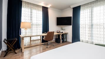 Una habitación de hotel con cama, escritorio, silla, televisor y cortinas.