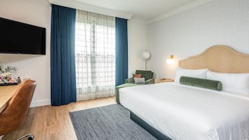 A hotel room with a bed, a desk, a chair, a TV, and a window with curtains.