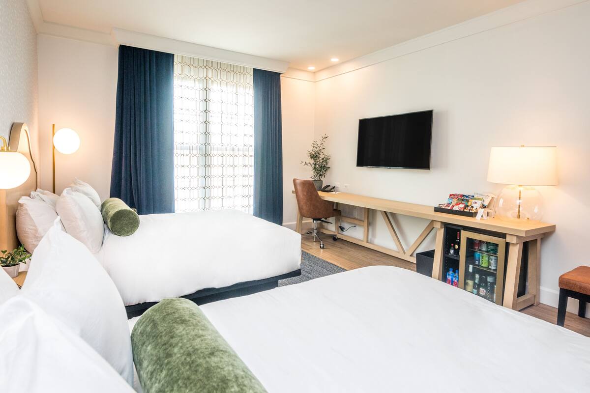 Habitación de hotel con dos camas, un escritorio, un televisor y un minibar.