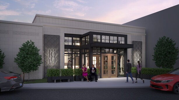 A modern building with a glass entrance, surrounded by greenery and a red car parked nearby.