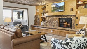 Ein gemütliches Wohnzimmer mit Kamin aus Stein, Ledersofas und einem darüber hängenden Fernseher.