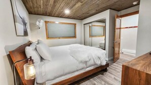 Ein Schlafzimmer mit Holzbalkendecke, einem Bett mit weißer Bettwäsche, einem Nachttisch mit Lampe und einem Spiegel an der Wand.
