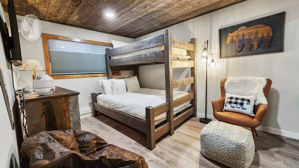 Habitación con literas, techo de madera, una silla con una manta de piel sintética y un cuadro con temática de osos.